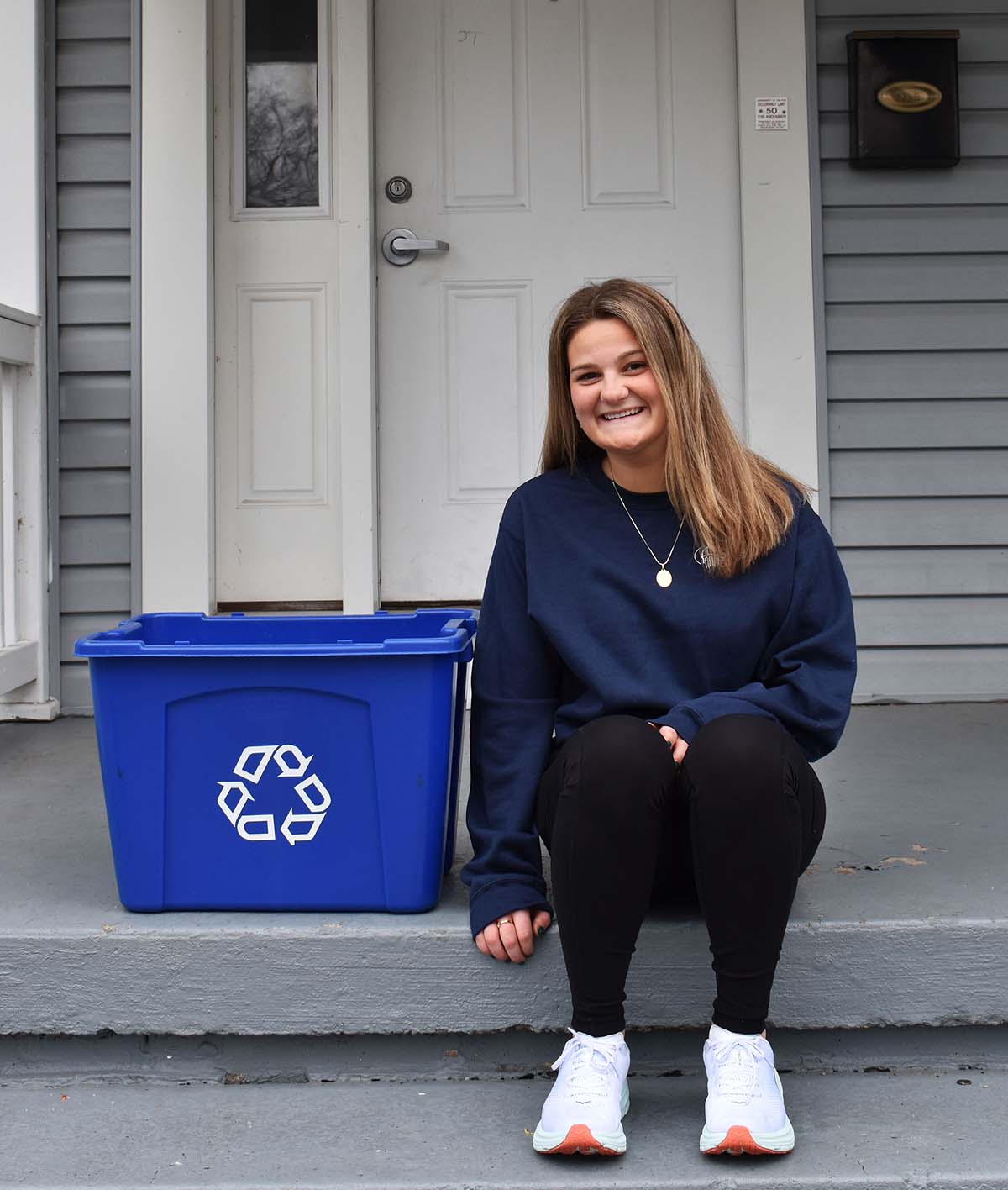 Student Hannah Hoby '22 sits on her front porch next to one of the blue recycling bins beside her.