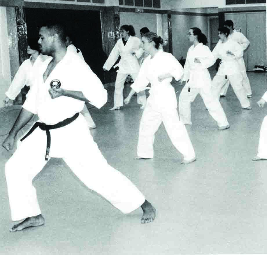 Several students doing kicks in mid-air during a karate class.