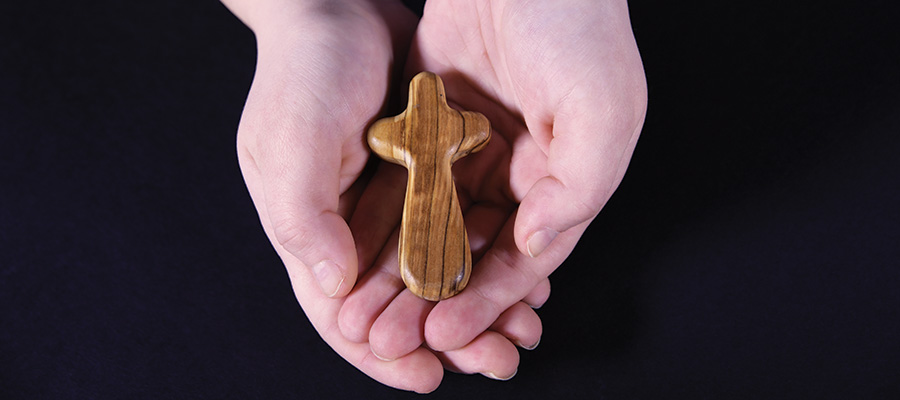 Child holds a small wooden cross cupped in their hands.