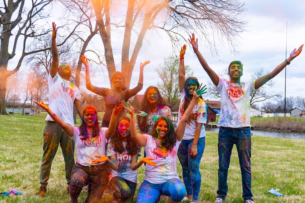 Students throw orange colored powder into the air and pose for a picture.