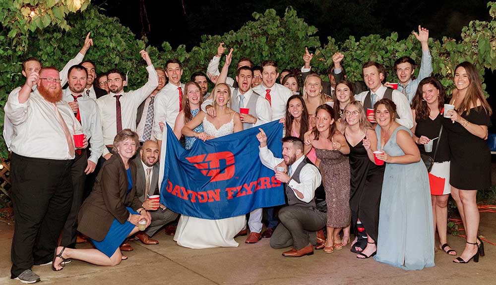 Wedding party holds up and poses with a Dayton Flyers flag.