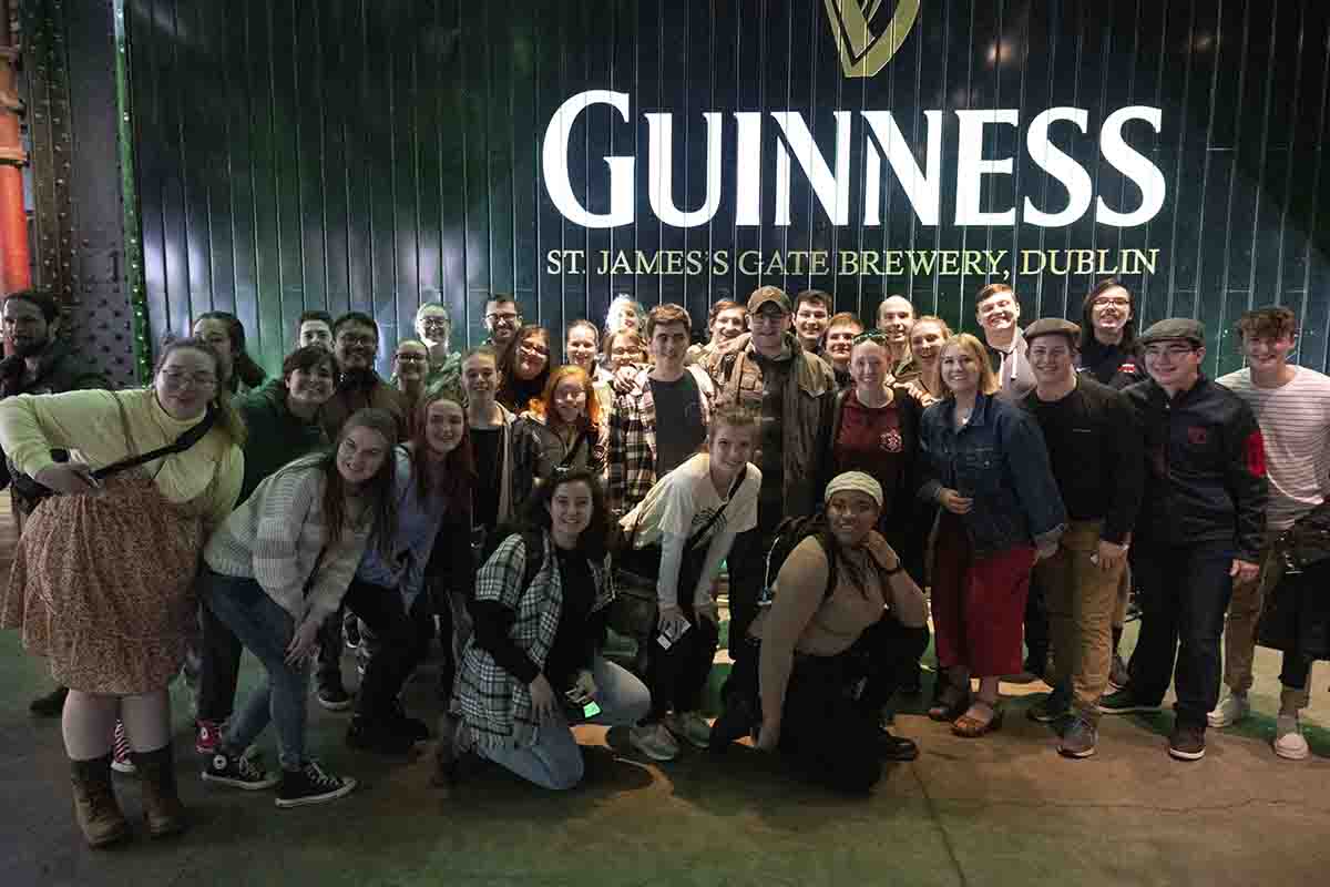 Pride of Dayton students pose in front of a Guinness sign.
