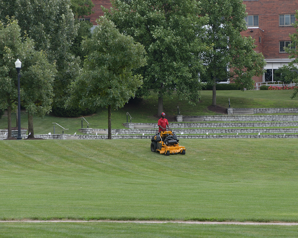 A facilities worker mows grass