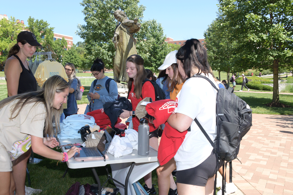Students surround a table at the at the Flyer Farmers' Market