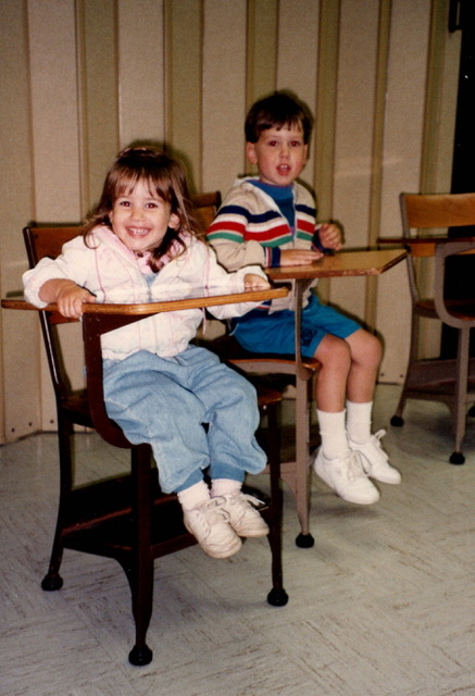 Two small kids sitting in school desks.