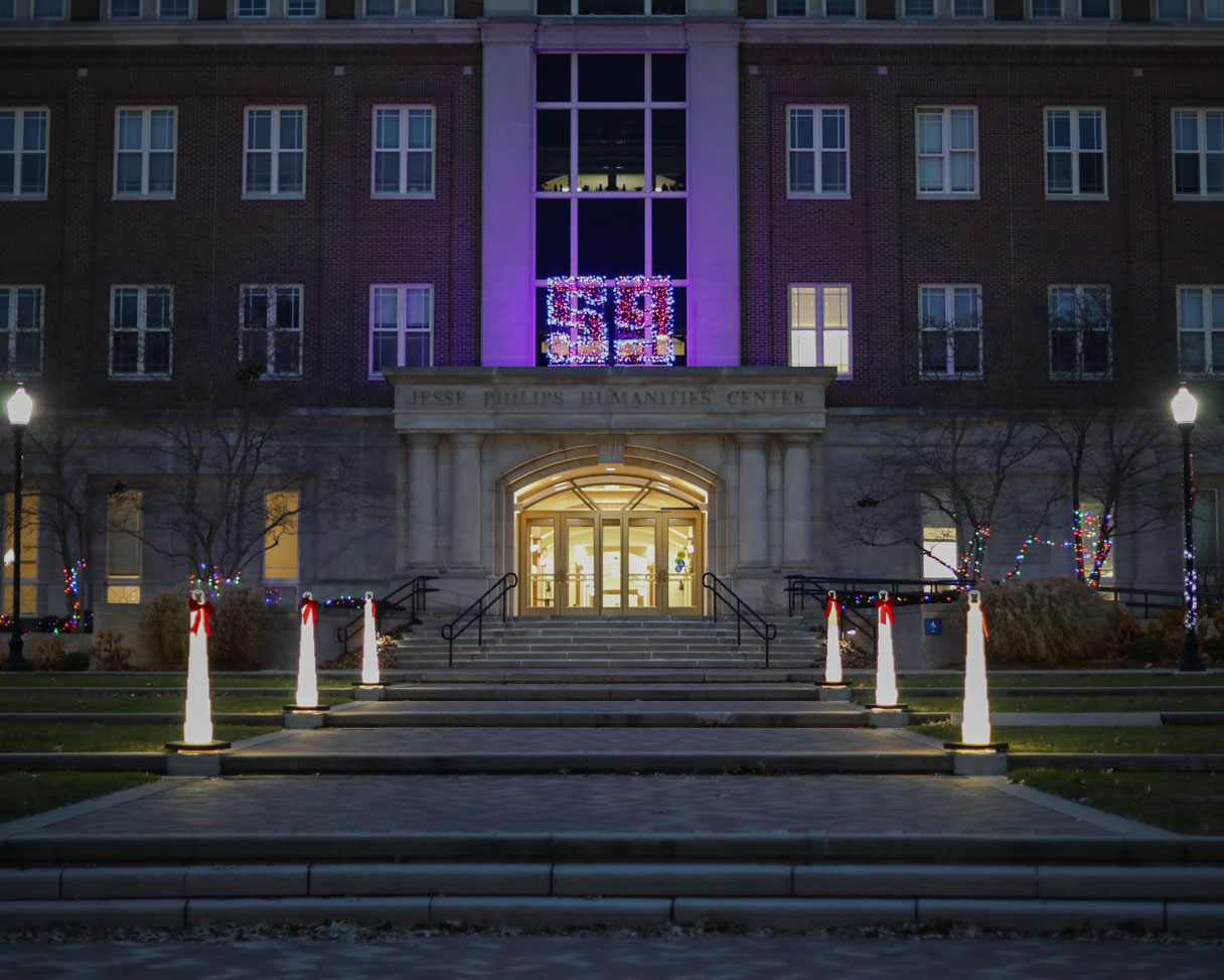 A path leading to the front of the JP Humanities building is decorated with white and multi-color lights.
