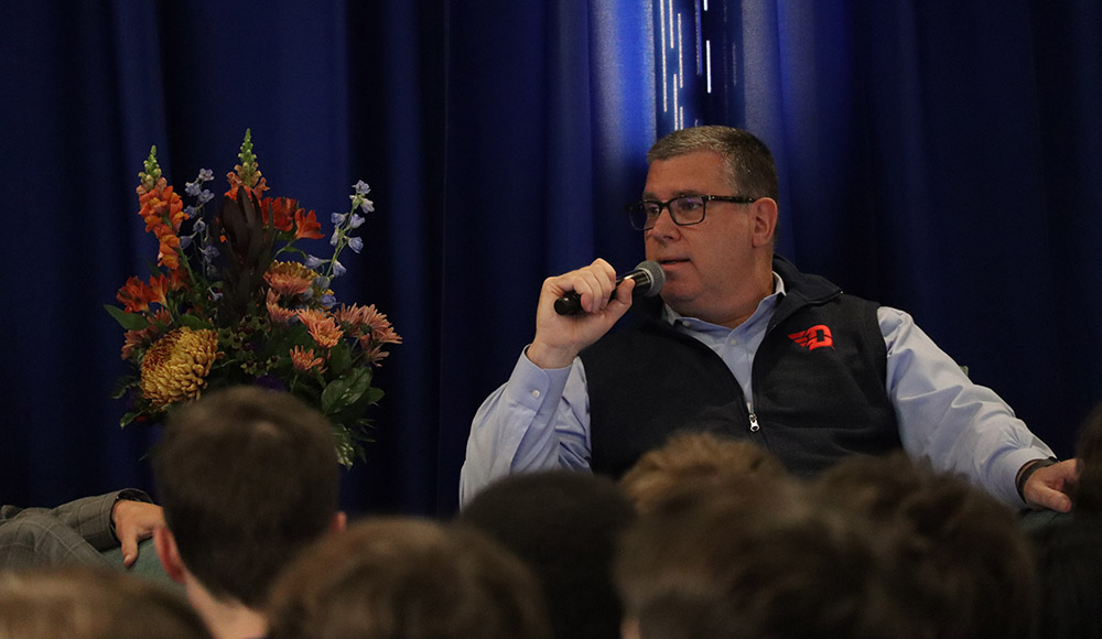 James Kavanugh holds a microphone while talking to students.
