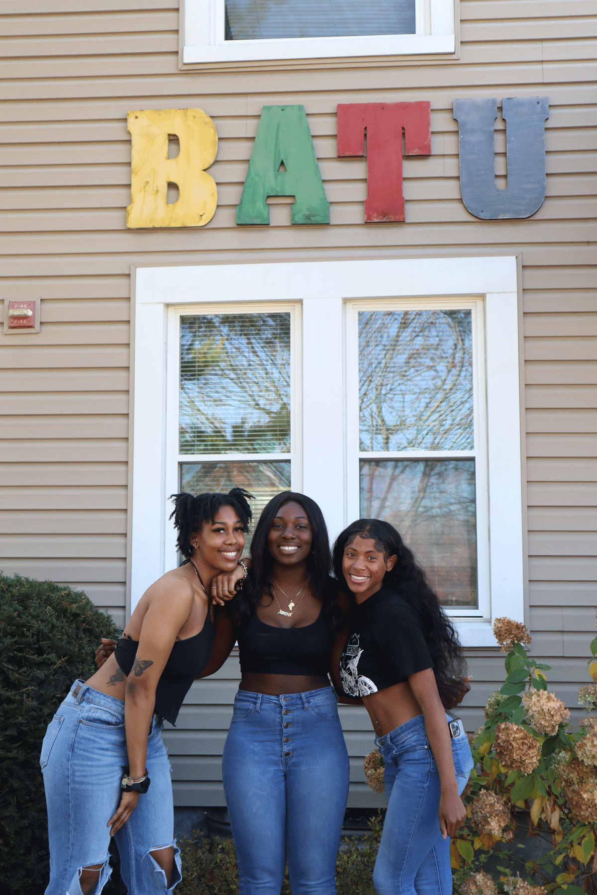 Three roommates stand in front of the house embracing.