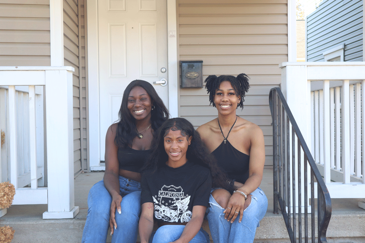 Three roommates sit on the porch steps together.