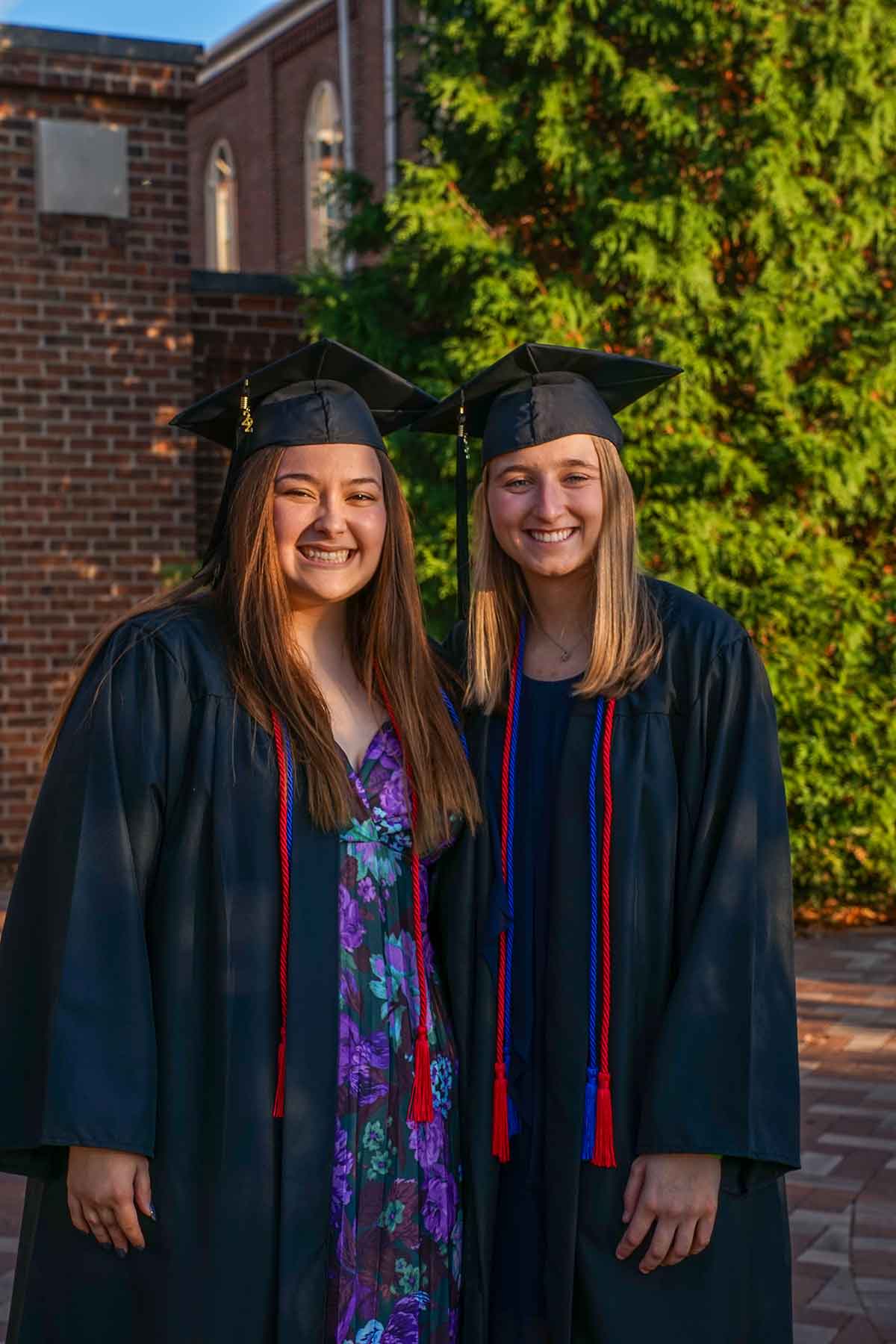 Two students stand in graduation gowns and hats