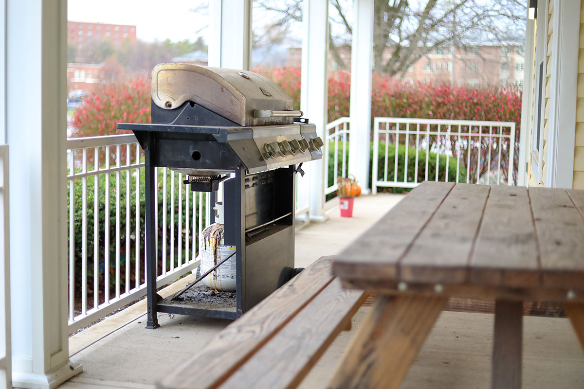 A grill sits on the front porch next to a picnic table.