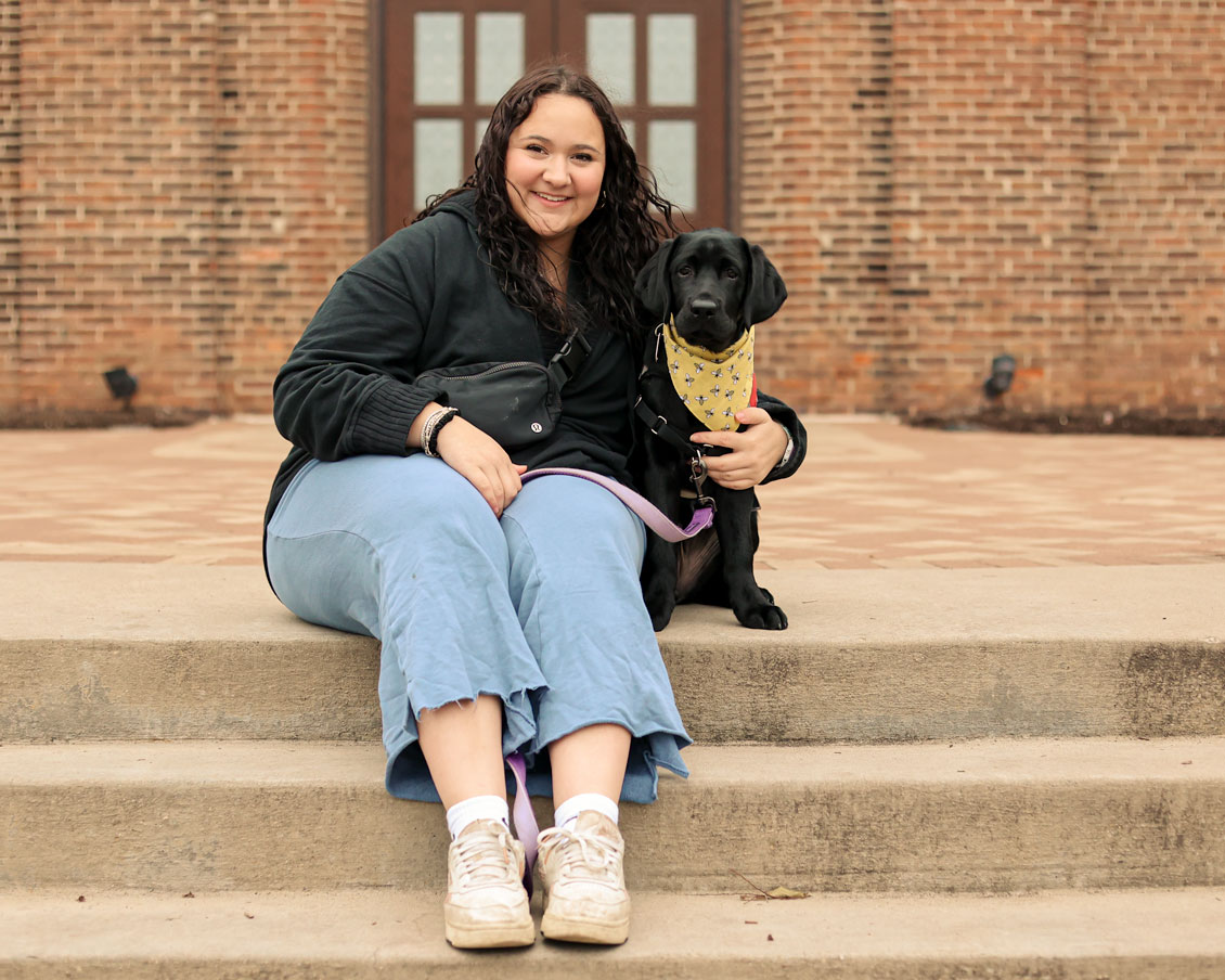 A student sits on the chapel stairs with her foster puppy, Ciara.