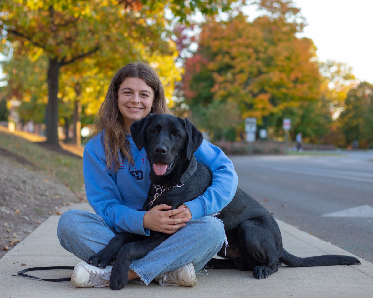 A student and her foster, Foxtrot sit on a campus sidewalk together