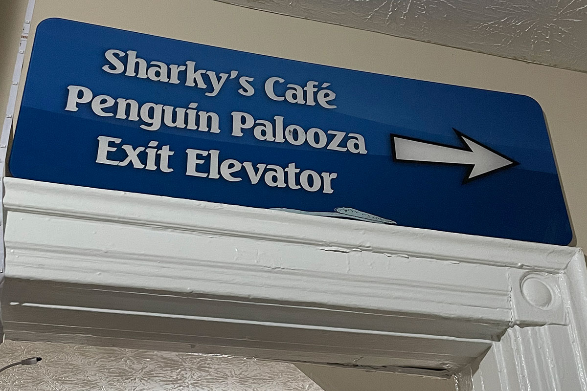 A sign that reads "Sharky's Cafe, Penguin Palooza, and Exit Elevator" with an arrow pointing to the right.
