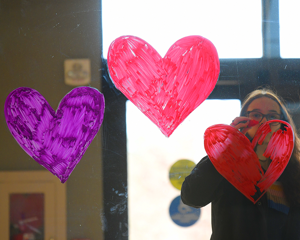 A student paints hearts on a window at The Hangar