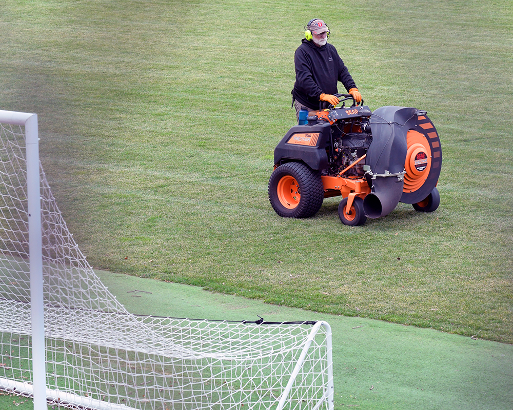 A worker uses a large blower to clear Baujan Field