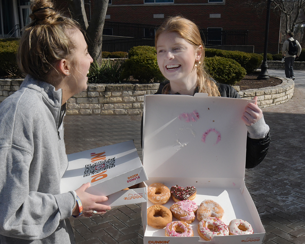 Two students hold boxes of doughnuts