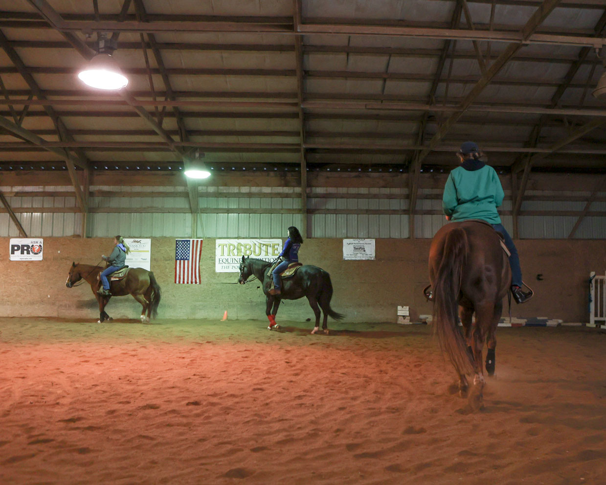 Three students each ride their horse around an arena