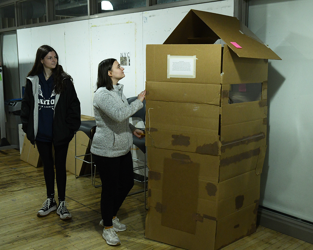 Two students work on an art project made with cardboard boxes