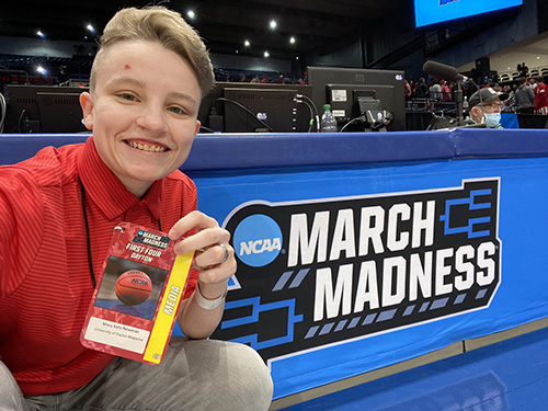 Author poses with March Madness signage holding up her Media badge.
