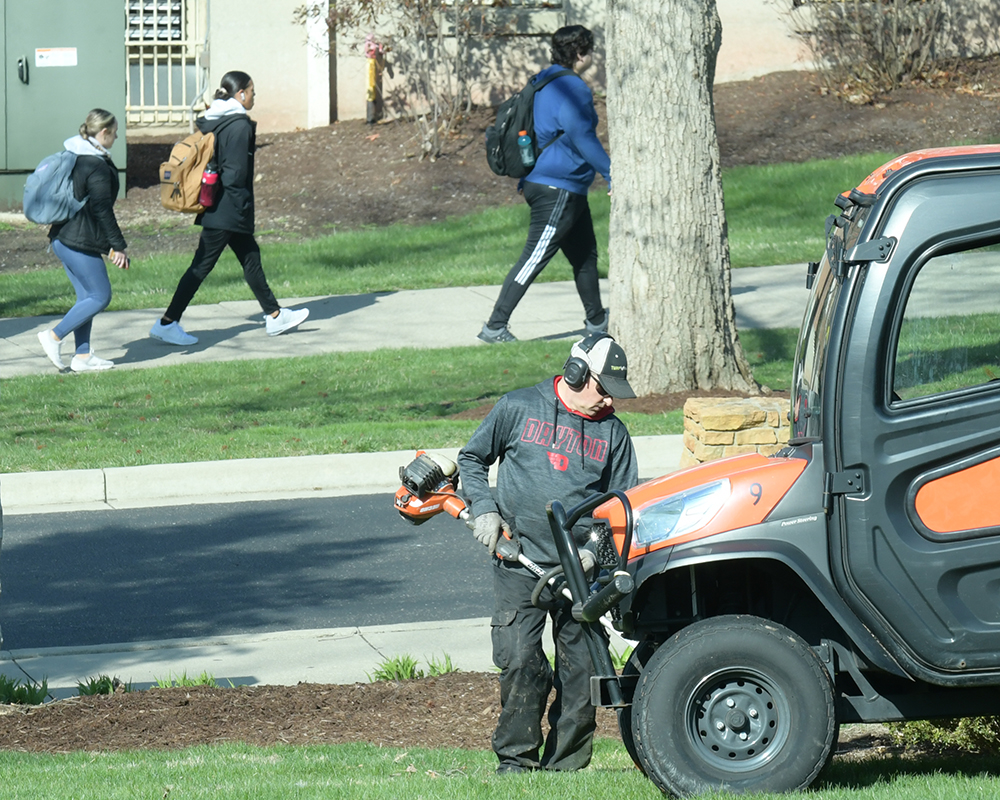 A grounds worker uses a grass trimmer