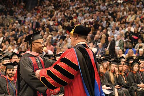 President Eric F. Spina shakes a student's hand at graduation.