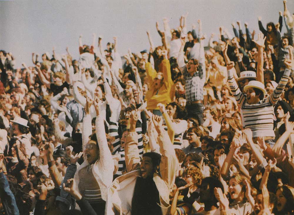 Large crowd of spectators standing and cheering at a game.