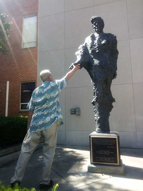 John Bunn reaches up to touch JFK statue's hand.