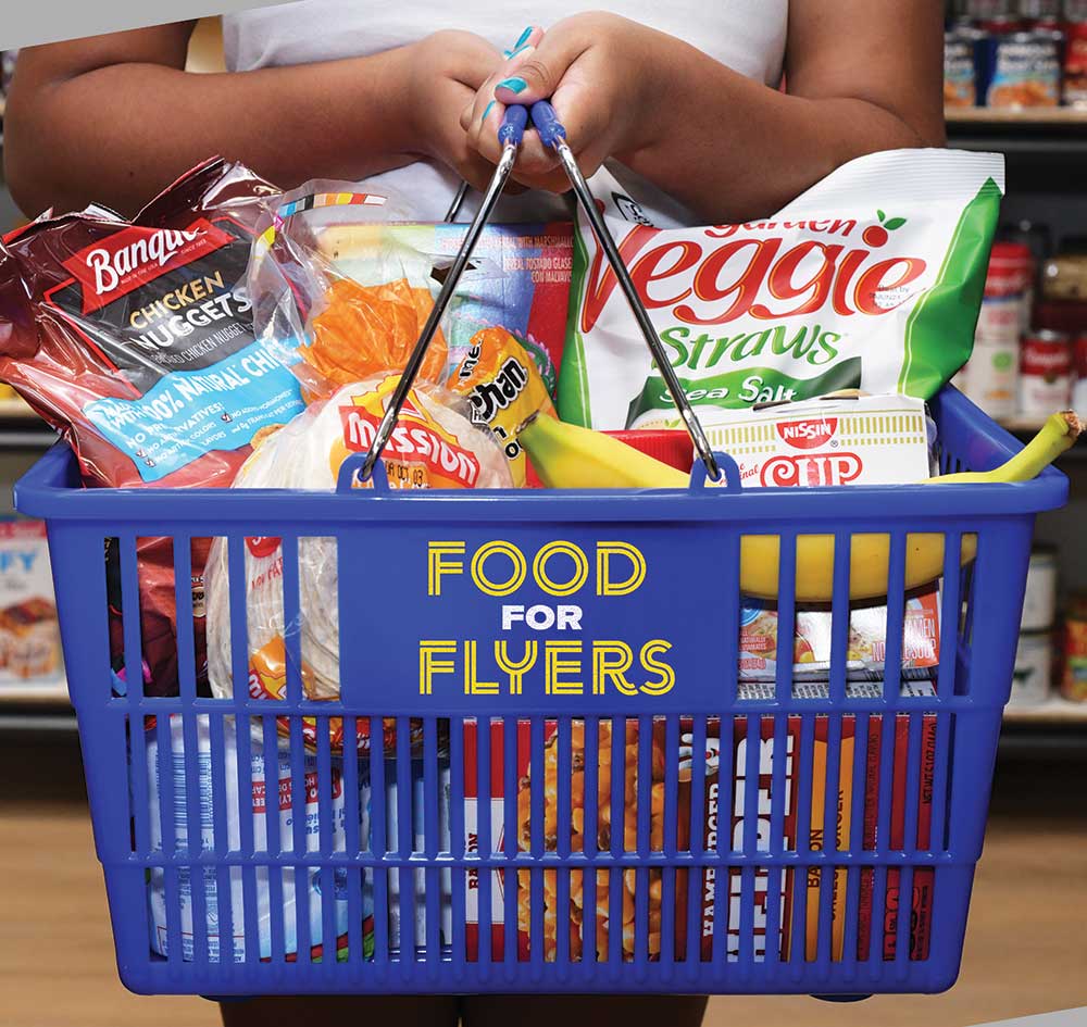 A grocery basket filled with food, a student holding it.