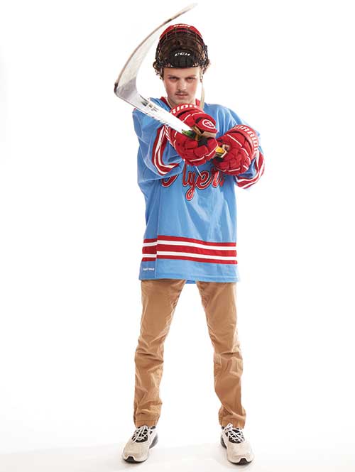 Hockey player points his hockey stick at the camera.