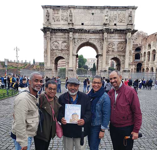 Alumni group stops to pose in front of an archway in Italy.
