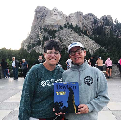 Two alumni stand in front of Mount Rushmore with a copy of the magazine.