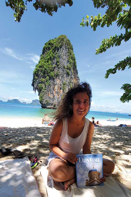 Alumna sits on the beach in front of Jeju Island holding the magazine.