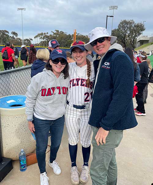 Norah poses with her parents at a softball game.