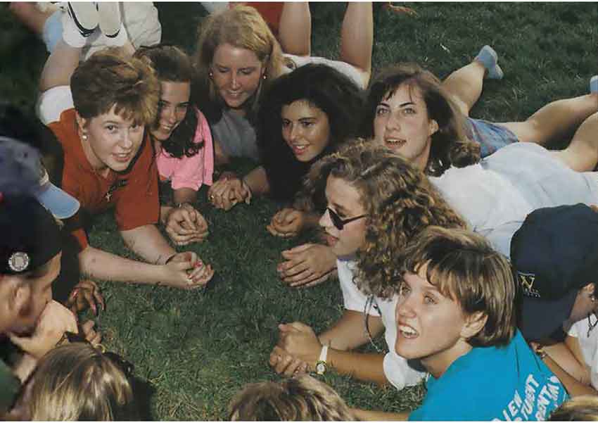 Female students all lay in a circle facing each other on the grass.