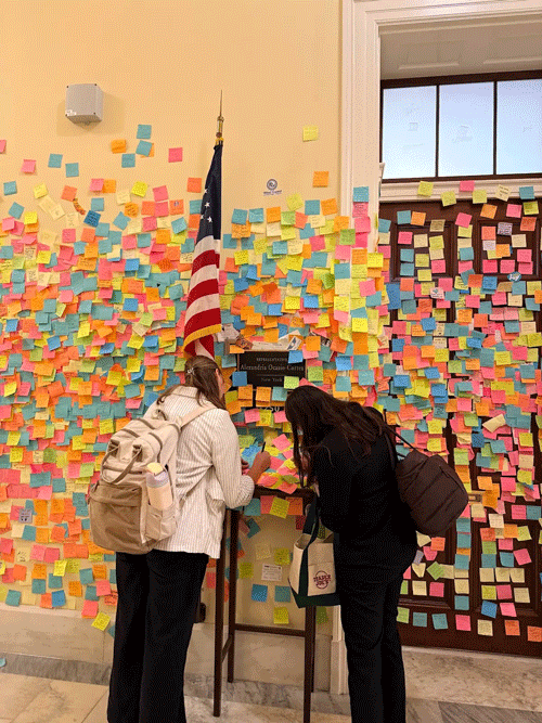 Karch and Guccione write post-it notes in a government building hallway.
