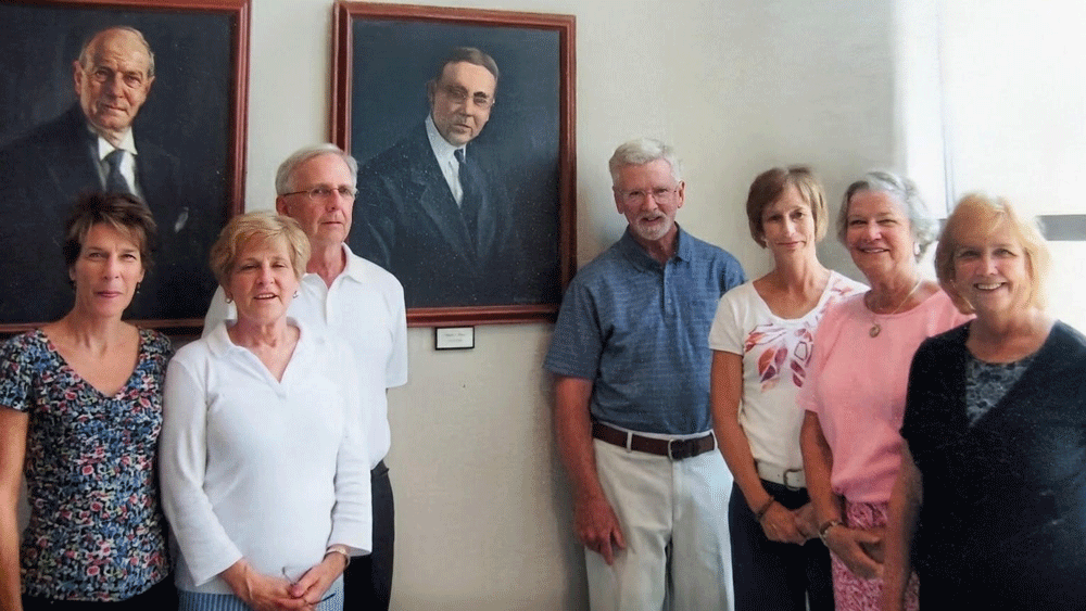 The family members stand in front of a portrait of their heir, John Shea.