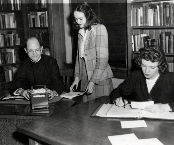 Father Edmund Baumeister, S.M. working with two female students at a table in a reading room