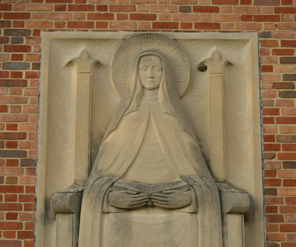 Bas relief of Mary looking straight ahead cradling an open book on her lap.
