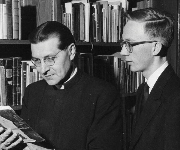 Hoelle on the left looking down and reading a book with Father Robert Maloy, S.M. looking over his should from the right.