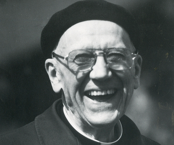 Father Theodore Koehler, S.M., wearing glasses and a dark beret, smiles as if laughing.