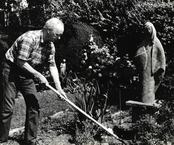 John S. Stokes tending to a garden near a statue of Mary