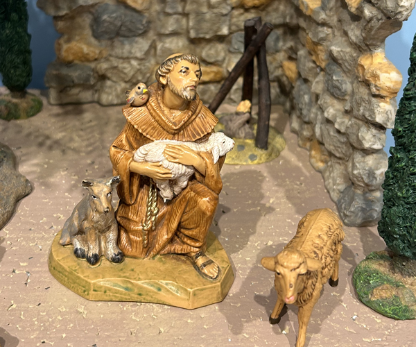 Figure of St. Francis clothed in a brown robe, sitting we a wolf to his right, a bird on his shoulder and a lamb on his lap. 