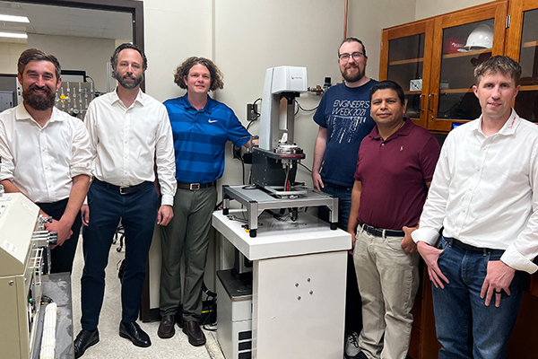 Six UD engineering faculty members standing with a new research instrument, three on either side of the equipment, in a lab setting.