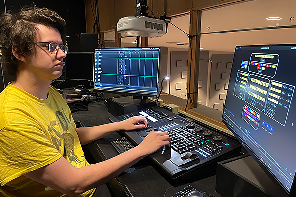 Nicholas Rollin sitting at the lighting control board in UD's Boll Theatre