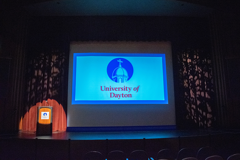 An empty stage with a spotlight on the podium and a powerpoint presentation displayed on a large projection screen