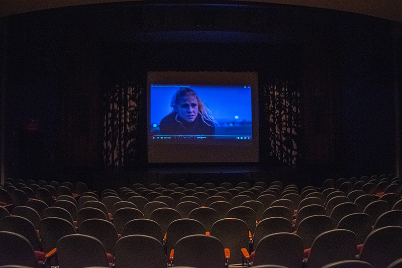 A view of the boll theatre stage from afar showing a movie being projected on a large screen