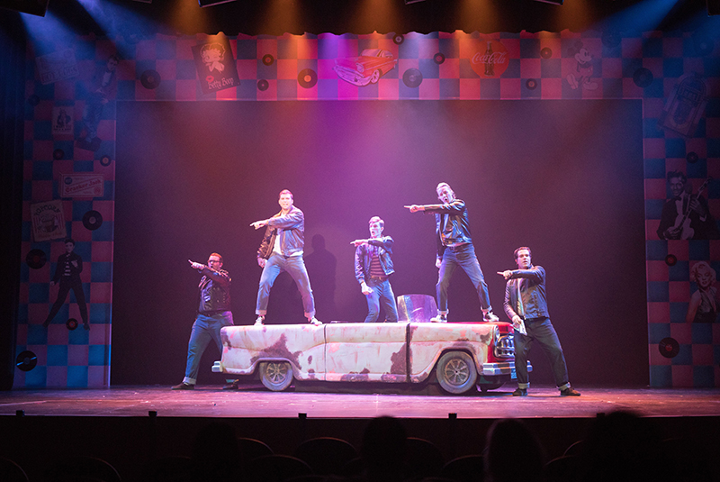 Five men dancing on and around a car during a musical