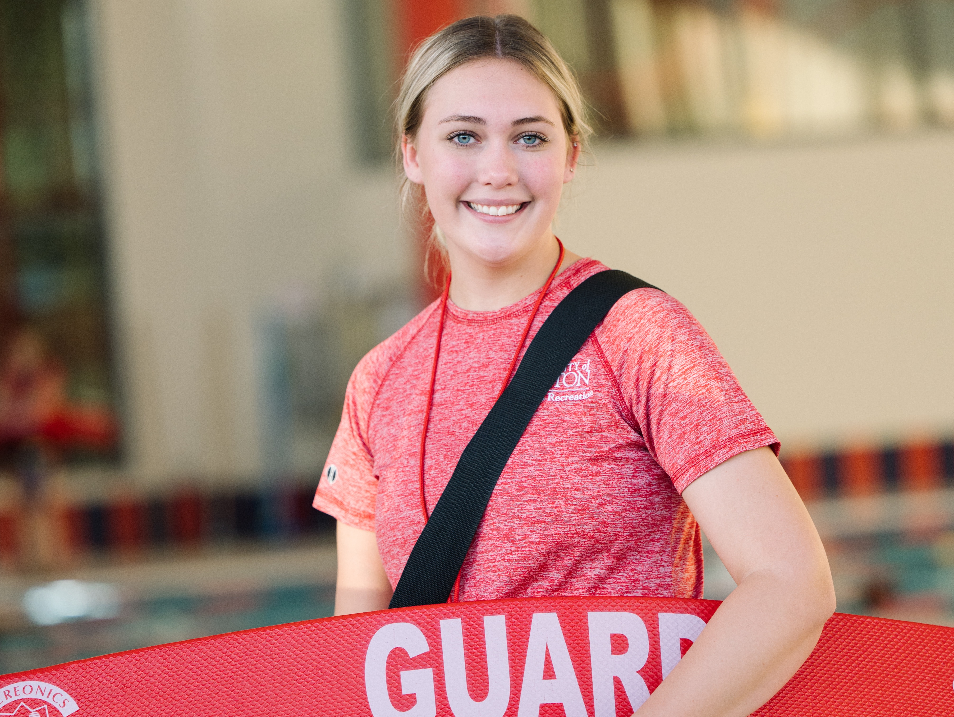 A student lifeguard in the aquatics center smiling on shift.