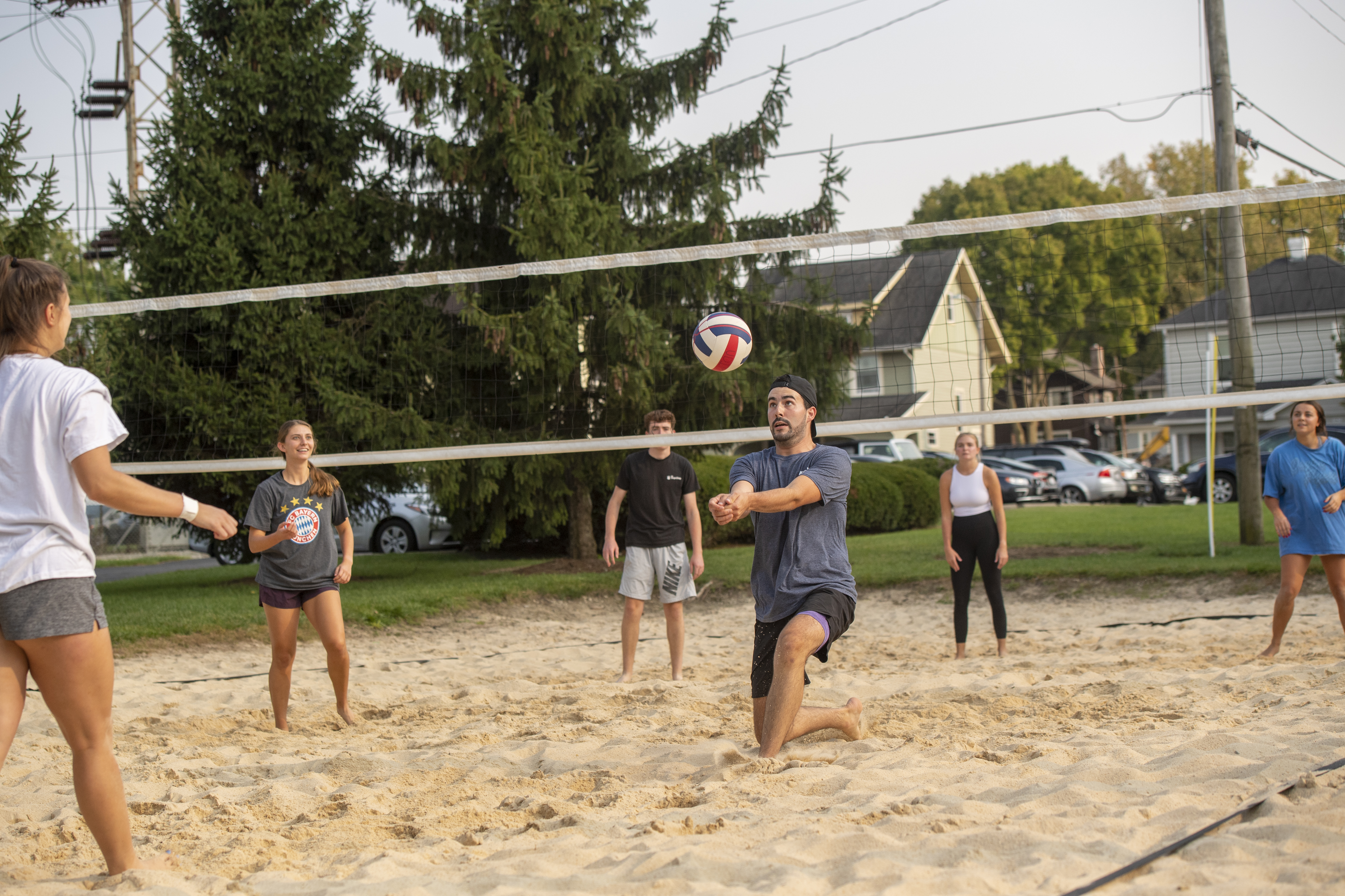 One male student bumps a volleyball to pass to his teammate as he plays sand volleyball with five other friends. 